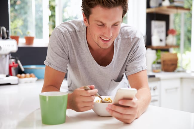 man checks email on phone while eating breakfast