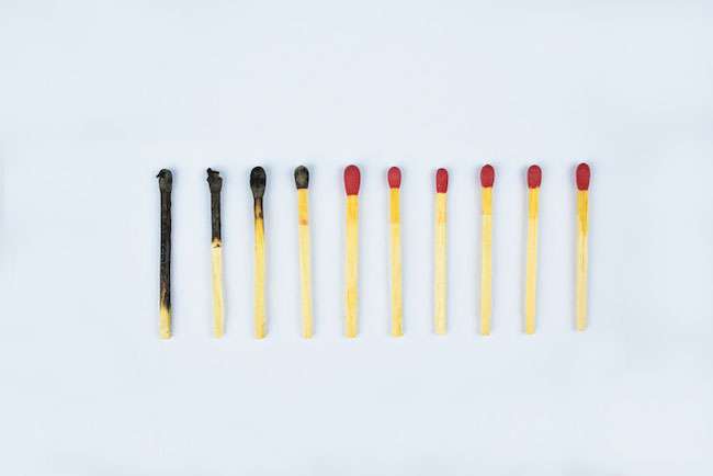 Ten burned matches arranged in a row showing the stages of a match burnt before a white background matches burned